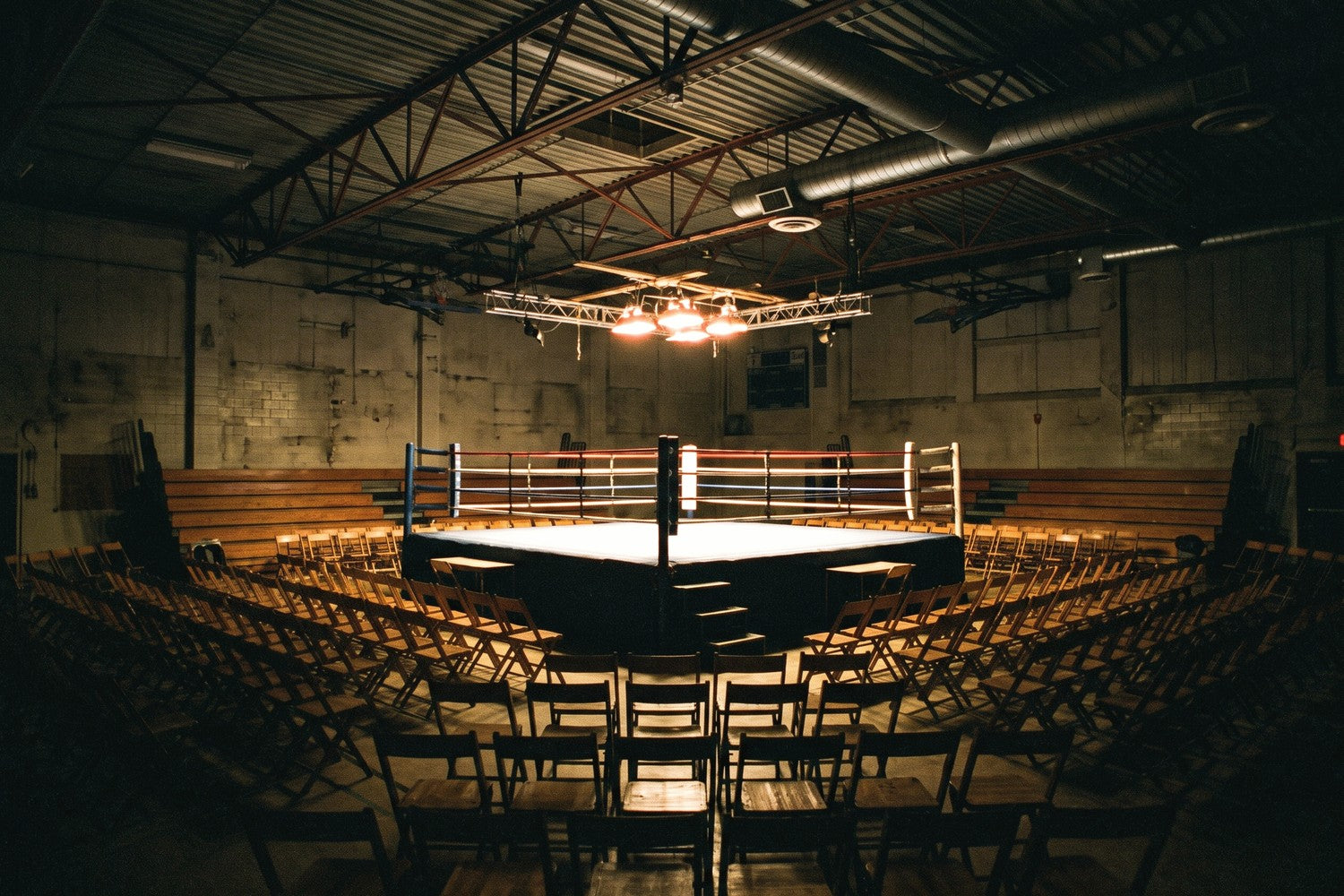 A small fight venue before the doors open, a lit ring in the middle with rows of empty seats around it