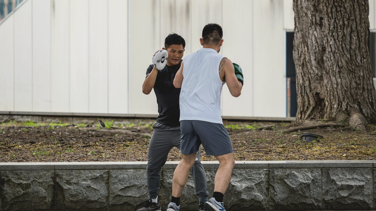 Two people doing boxing pad work outdoors under a tree